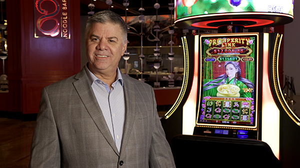 Paul smiling in front of a Prosperity Link cabinet on a casino floor