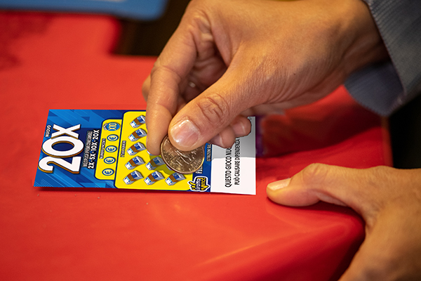 A hand scratching a blue and yellow instant ticket