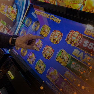 Hand touching IGT Fortune Coin Video Slot on touchscreen cabinet. 
